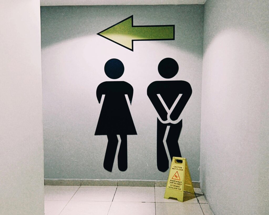 Moderne Wegweiser zu Toiletten in einem Einkaufszentrum in Almaty, Kasachstan, mit einem Warnschild „Nasser Boden“.