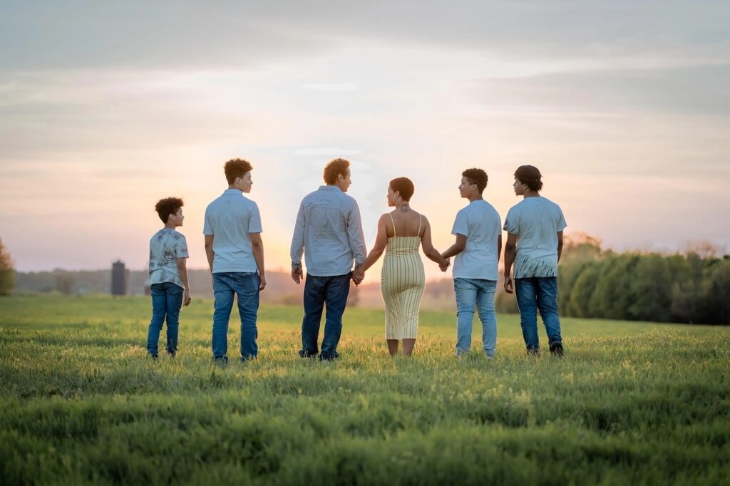Sechs Personen gehen Händchen haltend über eine grüne Wiese bei Sonnenuntergang.