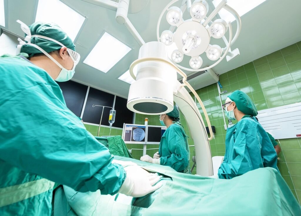 Chirurgisches Team in einem Operationssaal: Personen in grünen Kitteln, Hauben und Masken um einen abgedeckten Patienten und medizinische Geräte.