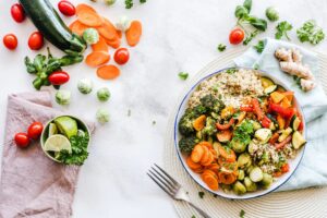 Schüssel mit Quinoa, Brokkoli, Karotten, Rosenkohl und anderem Gemüse, dazu Tomaten, Limette und frische Kräuter auf hellem Untergrund.